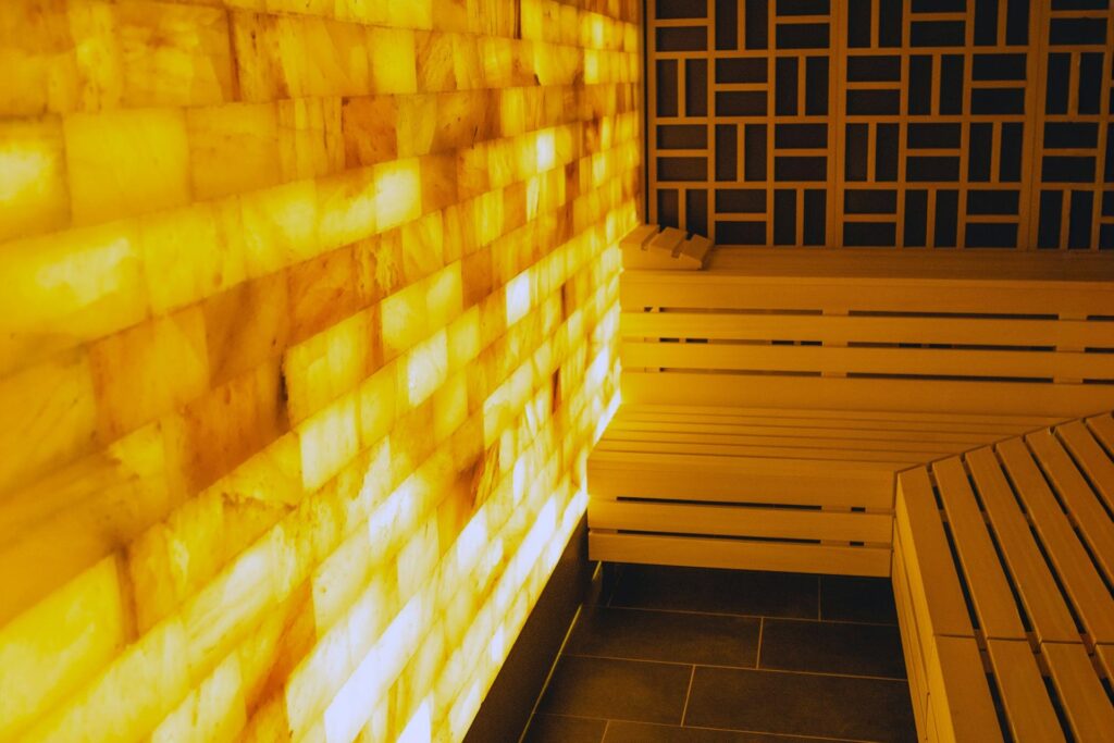 Leuchtende Salzsteinwand mit hölzernen Saunabänken in einer warm beleuchteten Salzsauna.